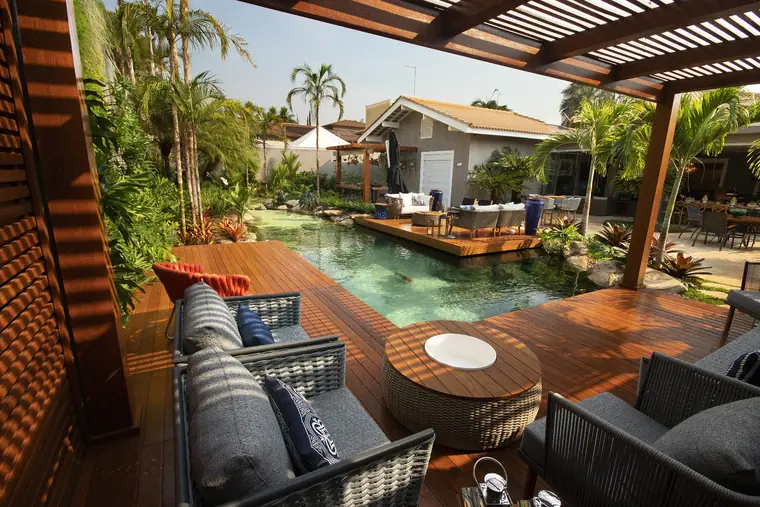 Deck com sofás à beira de uma piscina natural cercada por vegetação