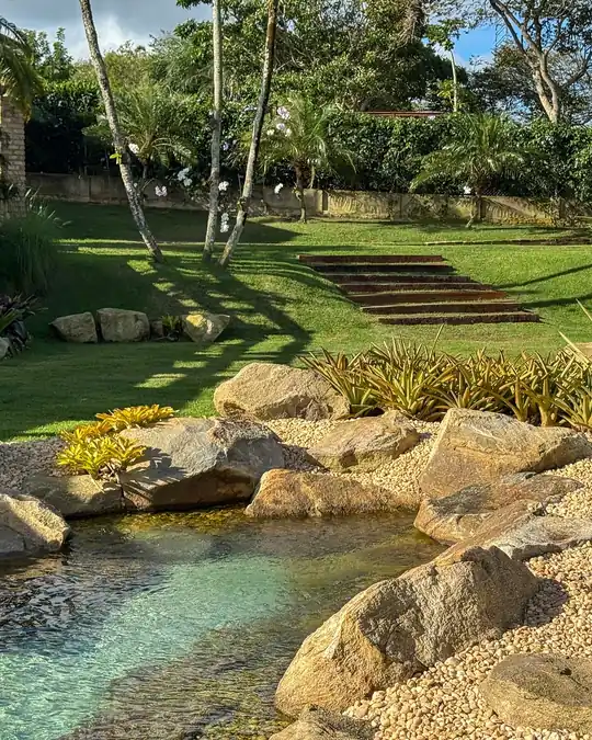 Lago de água clara entre pedras, com gramado e escada de jardim ao fundo