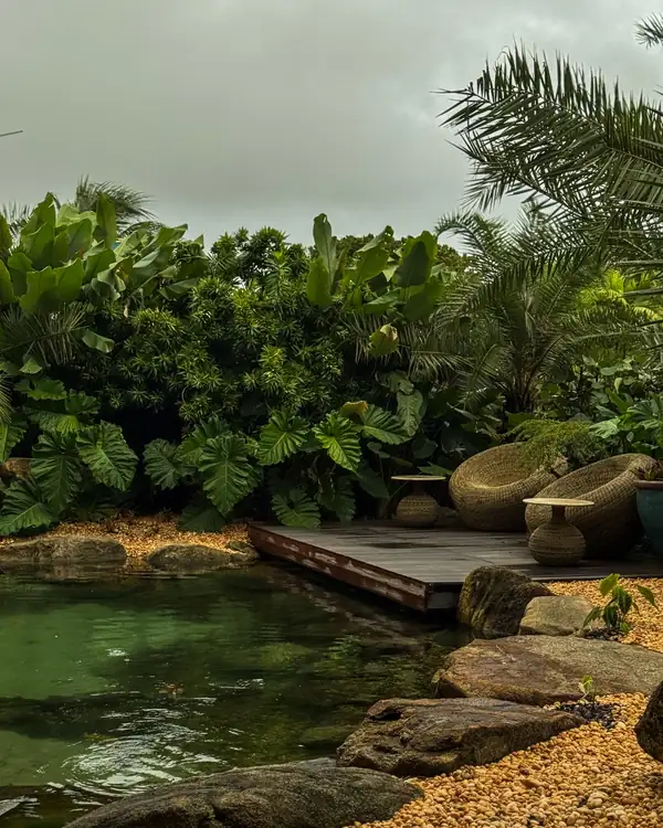 Lago residencial com deck, pedras e vegetação tropical em um dia nublado